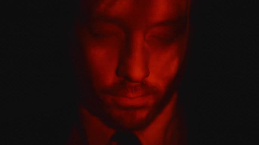 Red light wavers as it shines on a mans face in the darkness