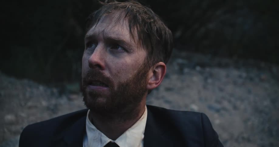 A soaking wet man shivers while sitting along a rock wall