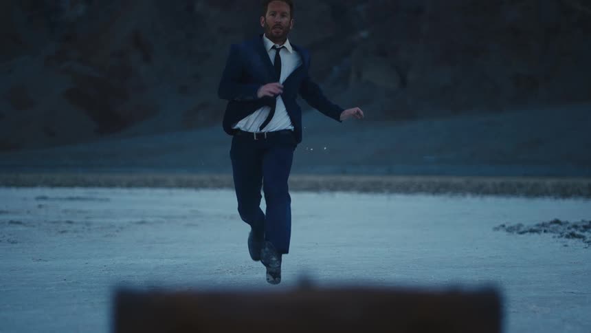 A man in a suit running toward a suitcase on the beach