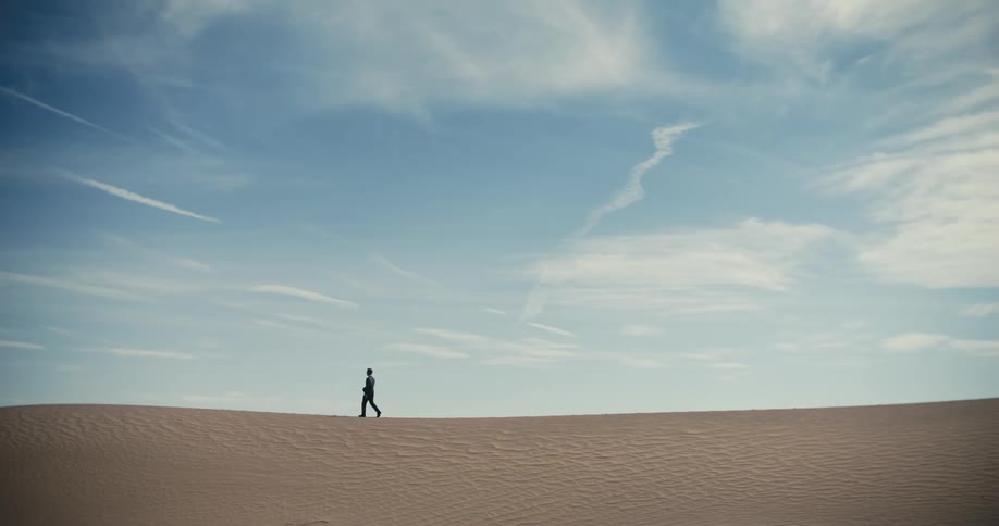 A man is walking across the desert under a cloudy sky