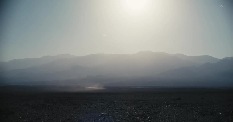 The sun shining down on a barren landscape with mountains in the distance