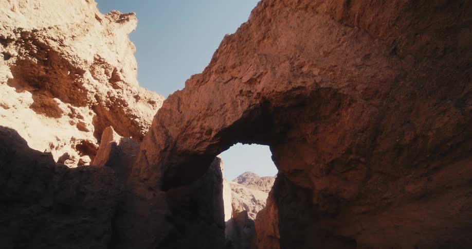 Sun shines on top of cliff and on mountain visible through shadowed arch