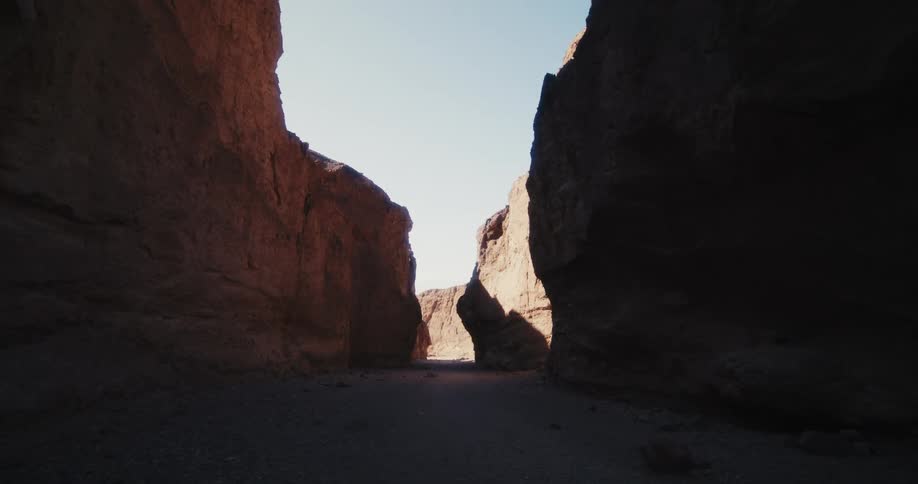 The majority of the area between rock walls remain in shadow under a clear sky