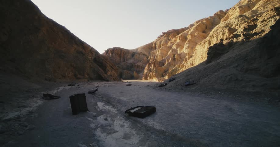 Empty cases and bags are strewn across dirt path between bare rocky hills