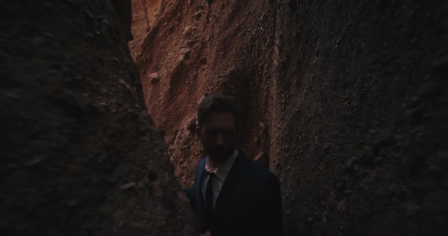 A man in a suit walks through the a narrow crevice on the floor of a canyon during the day