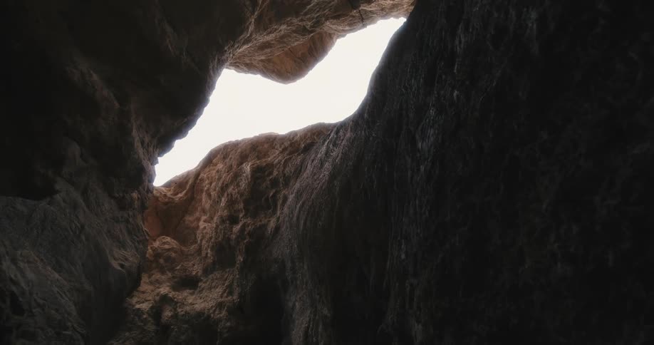 Narrow path through cavern opens to show sky through gap