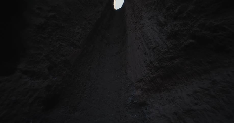 Man wearing business suit stands looking up gully wall toward sky showing through gap