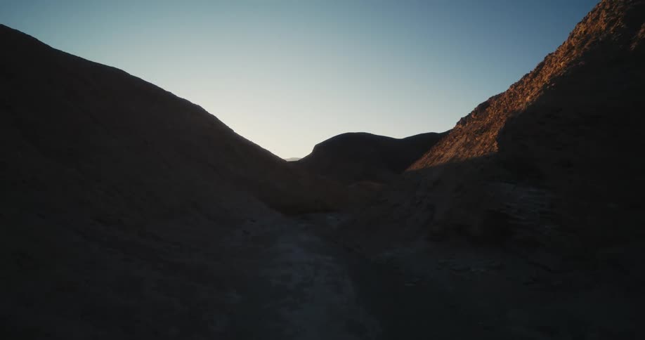 Narrow path of ground winds between shadow hills under a clear blue sky