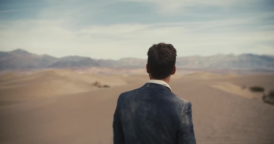 Dust coated man walk across desert toward mountains under a cloudy sky