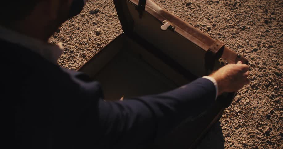 A man wearing a suit is sitting in the desert sand as he opens a briefcase and it is empty