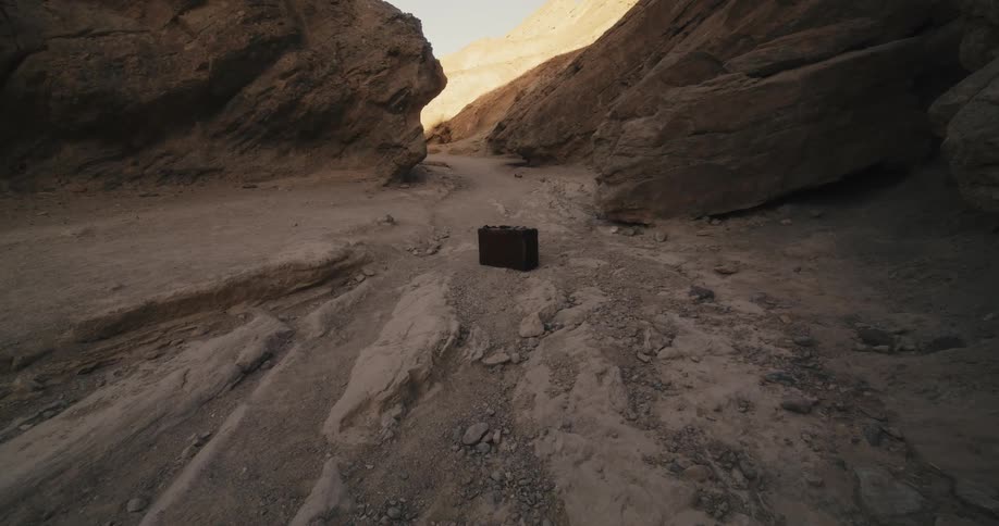A briefcase is standing up on the desert soil among rocks near mountains