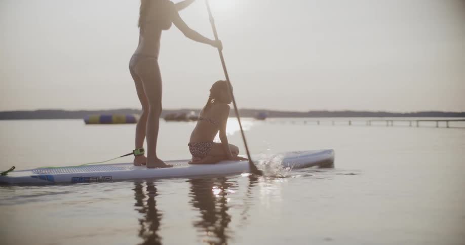 A woman and girl on a paddle board paddling in a bay