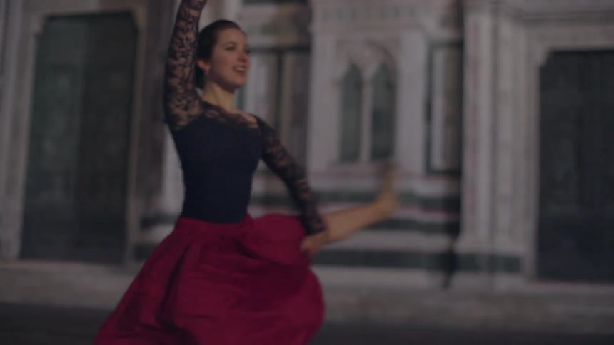 A woman dances in front of an ornate facade