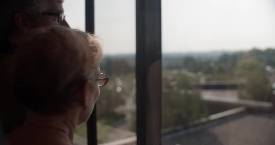 Two people look out of a window as they ride an elevator