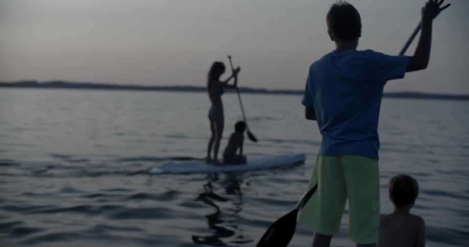 A family on three separate paddle boards paddles at dusk