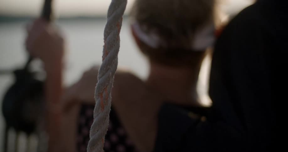 A man and woman stand on a sailboat in the evening