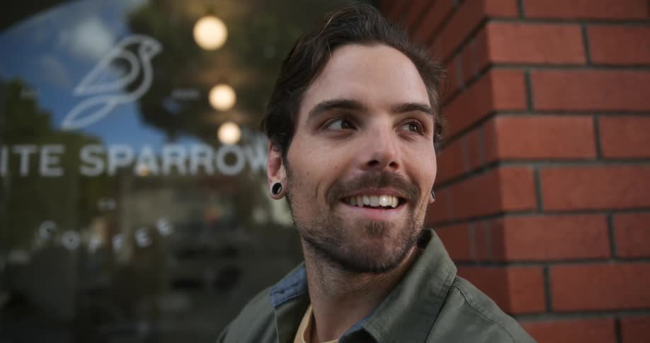 Man wearing green shirt and ear tunnel plugs talks with person in front of cafe