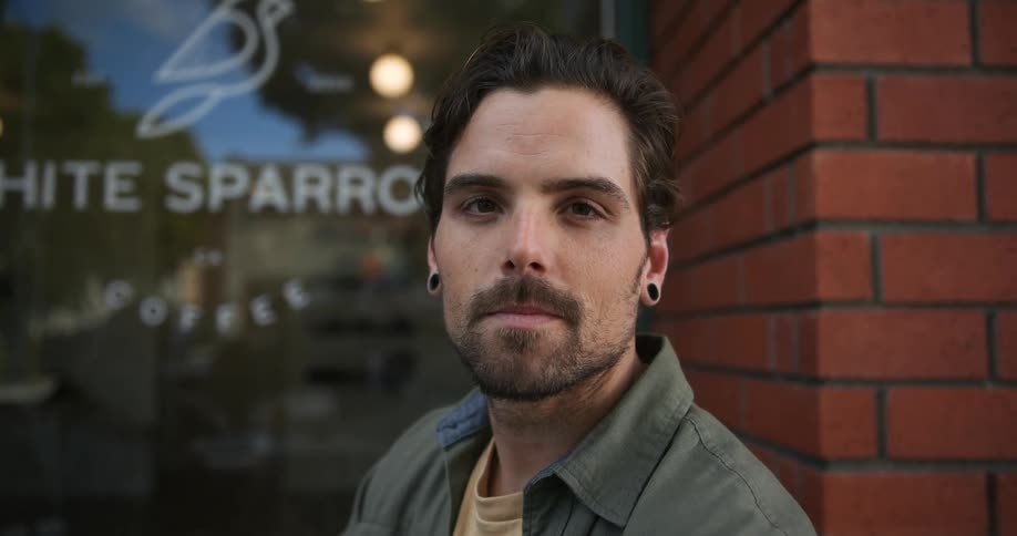 Young man standing on the front entrance of a coffee shop looking at the camera