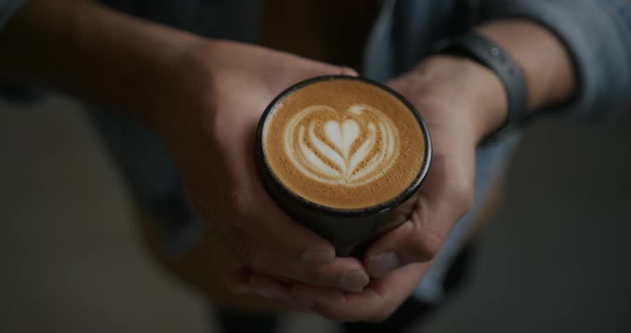 A man is holding a cup of coffee with a heart design in the foam