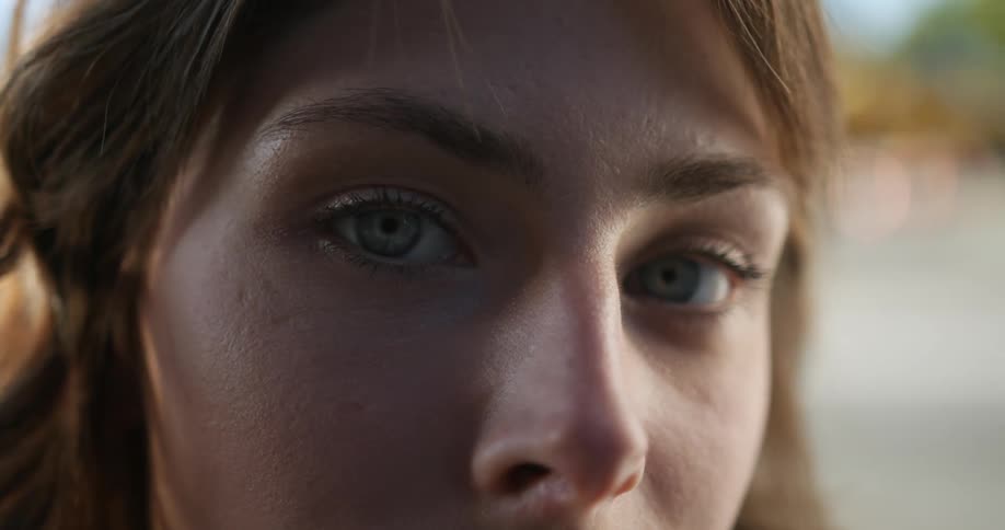 A woman standing outdoors slowly opens her eyes to look into the camera