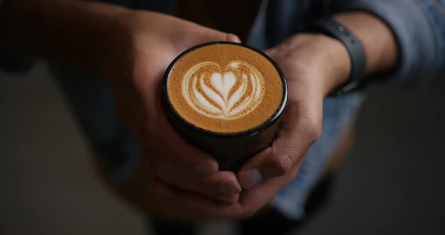 Barista shows a cup of coffee with latte foam art to the camera