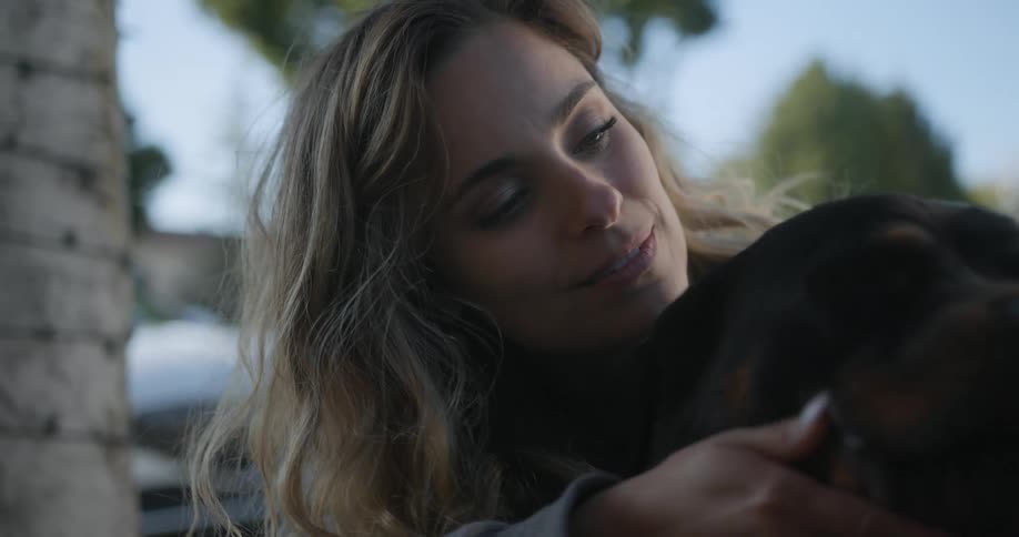 Woman with brown hair and green eyes pets and kisses black dog in the street