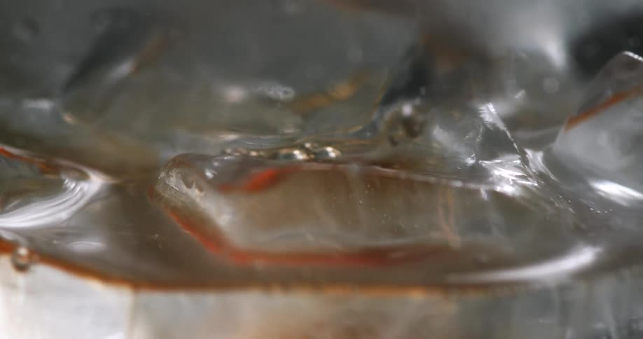 Close up shot of brown drink pouring over ice then mixing it
