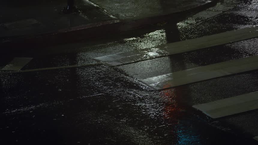 Rain falling at night on crosswalk near gutter