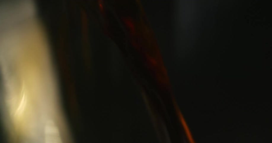 Brown beverage flows into clear container wetting side and making it shine