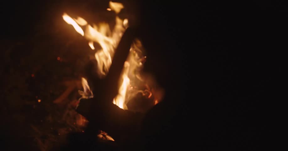 Person silhouetted against campfire leans head against object