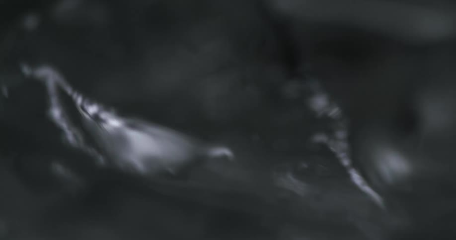 Extreme close up of ice cubes on the surface of a clear drink being stirred
