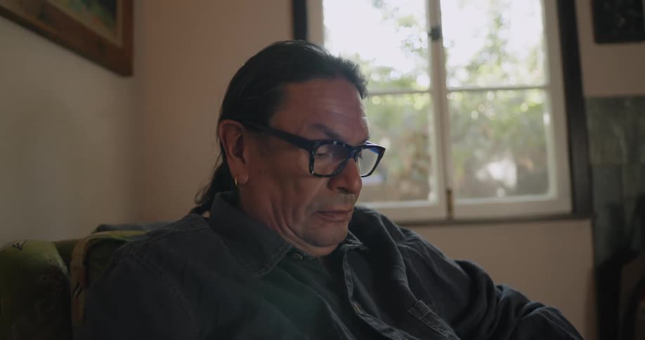 Man wearing glasses sits on a couch at home reading