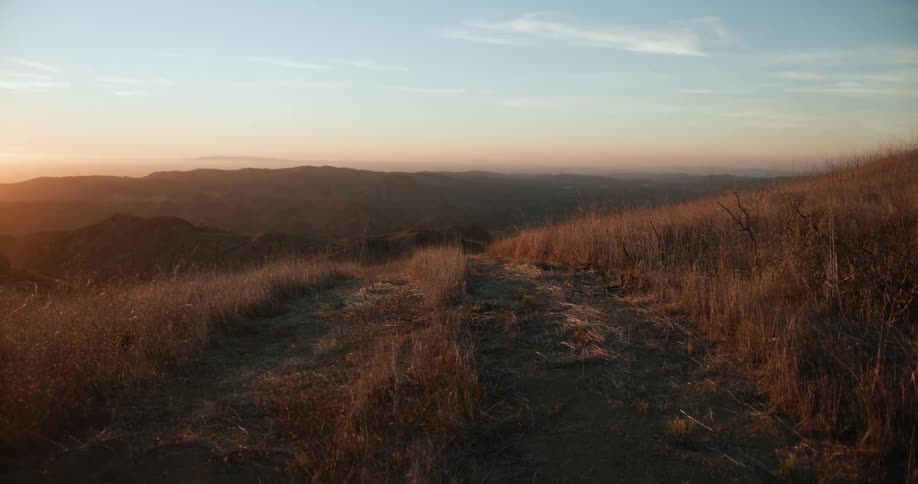 Landscape of country road leading down hill slope at sunset