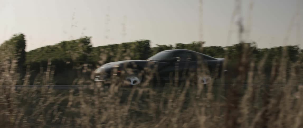 Black sports car drives on country road at sunset