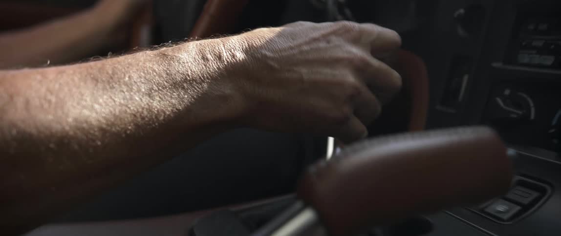 A man reaches to shift gears as he drives a car