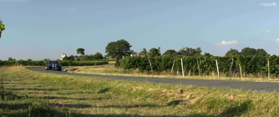 A sports car with stripes driving on a paved rural road