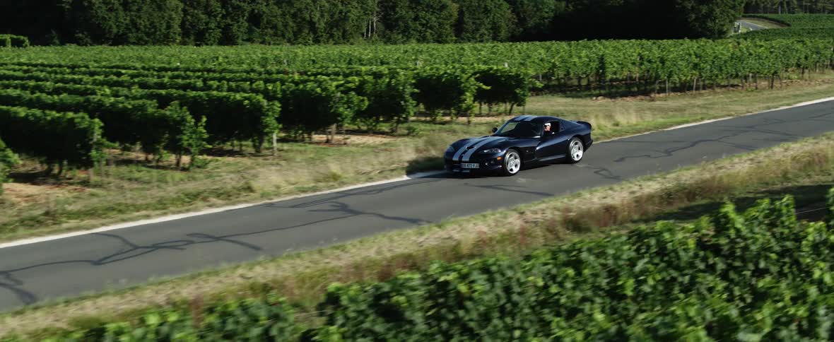 A black sports car is traveling on a rural road through farmland