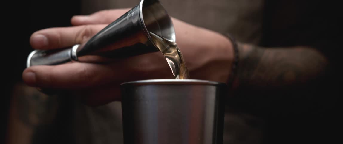 A person pours liquor from a jigger into a shaker