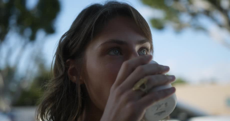 Woman drinking coffee outdoors and looking off to the distance