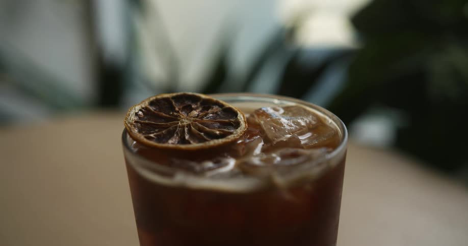 A person garnishes a cold coffee brew with a slice of lemon