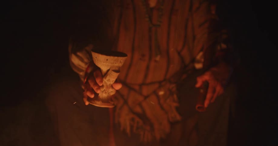 A man lowers a goblet into a campfire