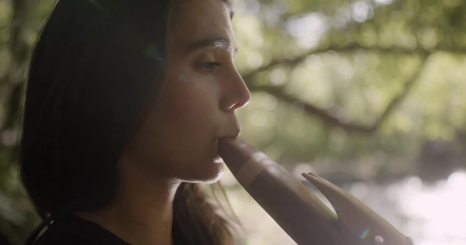 A woman plays a traditional wind instruments while sitting outdoors during the day