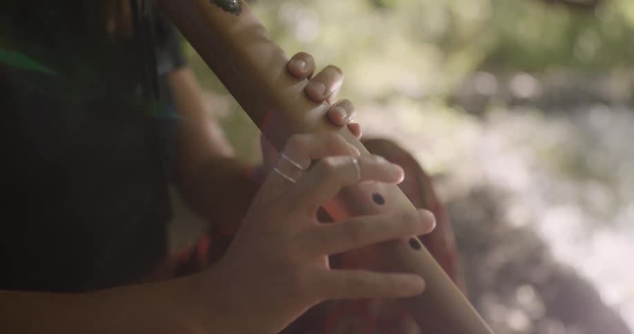 A person sits outdoors playing a flute like wind instrument