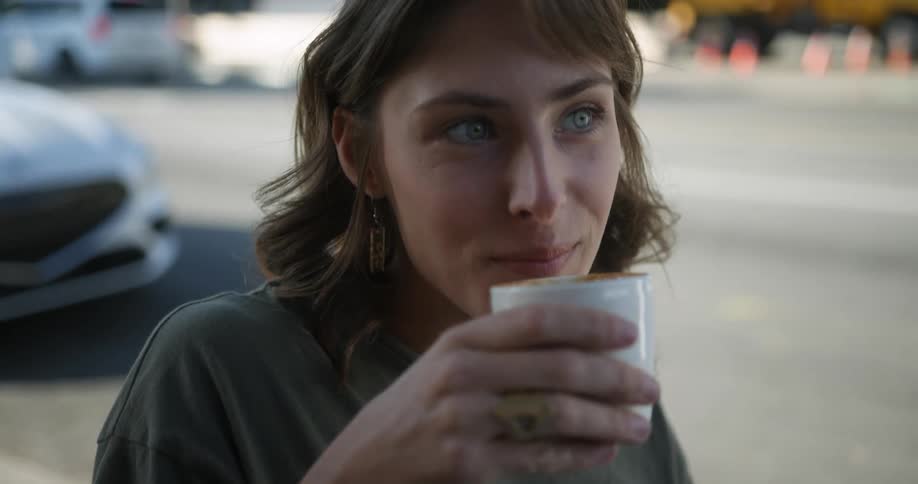 A young white woman is drinking some coffee outside in a small town