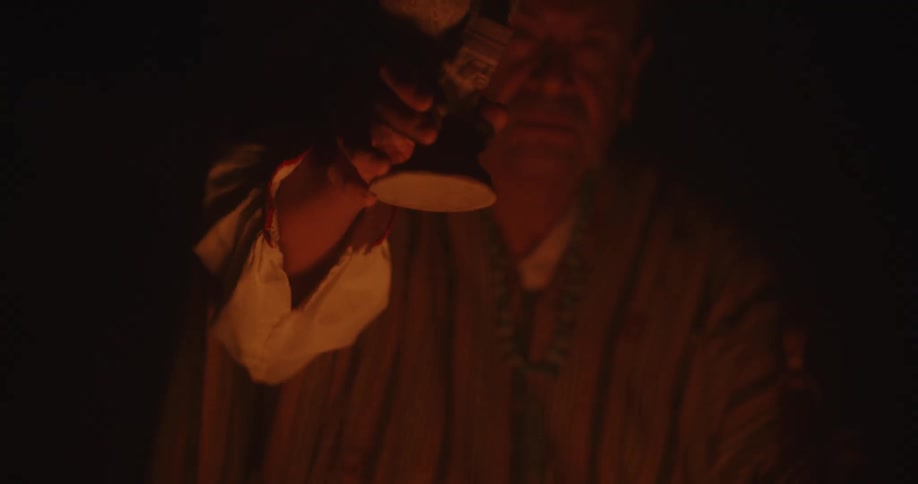 A man holding up a clay cup next to a burning bonfire