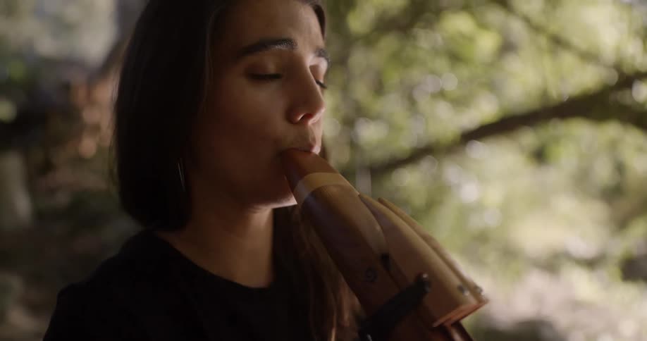 A woman plays a woodwind instrument outdoors during the day