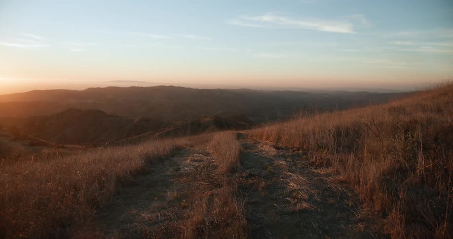 Landscape of country road leading down hill slope at sunset