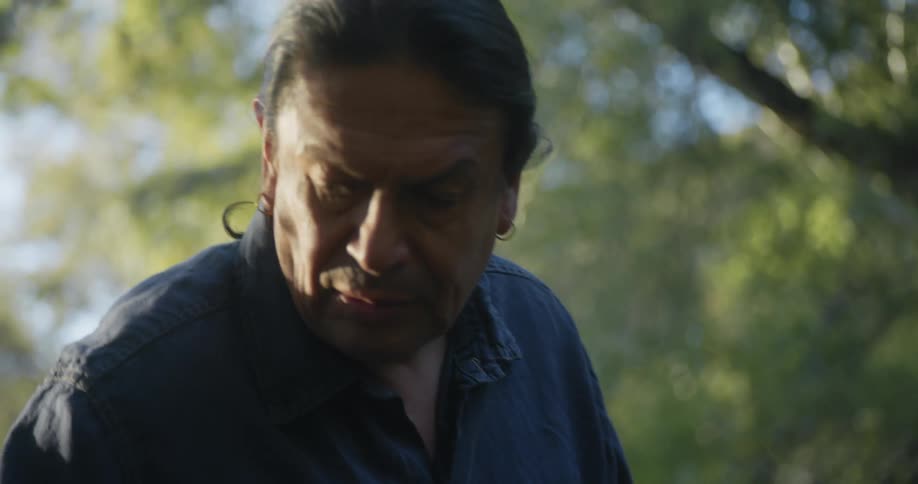 Man wearing a ponytail carries his bags to a table in the backyard at evening