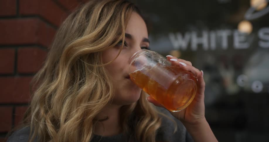 A woman sits outside a restaurant and takes a drink of a beverage
