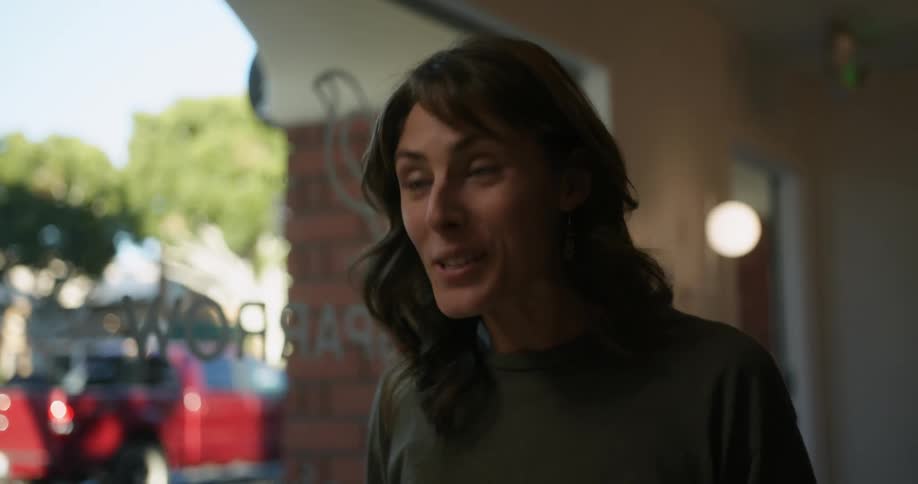 Woman with green eyes brown wavy hair and green t shirt enters cafe and says hi